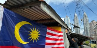 A resident of Kampung Baru proudly displays the Jalur Gemilang in front of his home, honouring Malaysia's national pride.